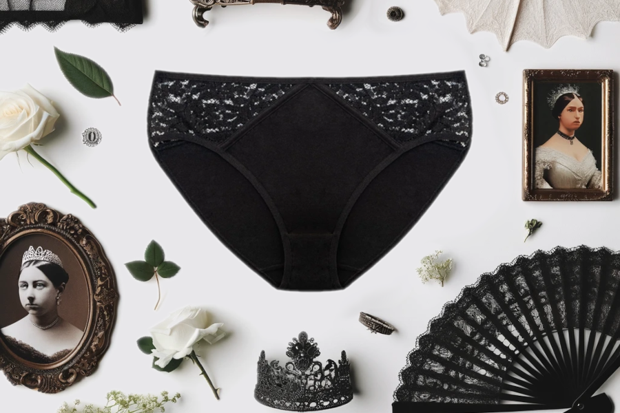 Flat lay image featuring the black lace brief 'Alexis' from Candis, surrounded by elegant accessories including a delicate tiara, a vintage black lace fan, white roses, and portraits of Queen Victoria, highlighting Queen Victoria’s fashion.